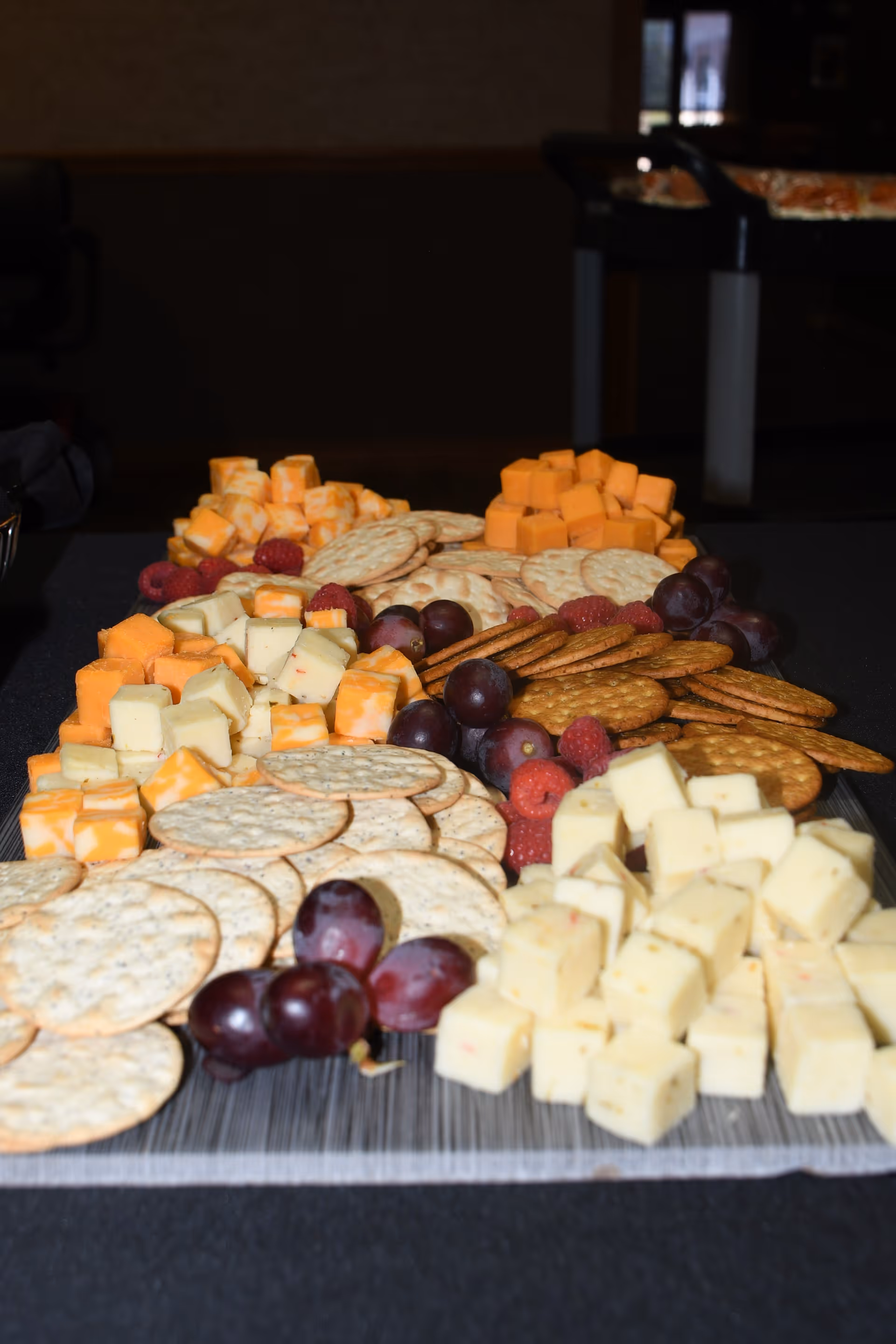 A close-up view of a platter with an assortment of cubed cheeses, round crackers, red grapes, and raspberries arranged neatly on a table.