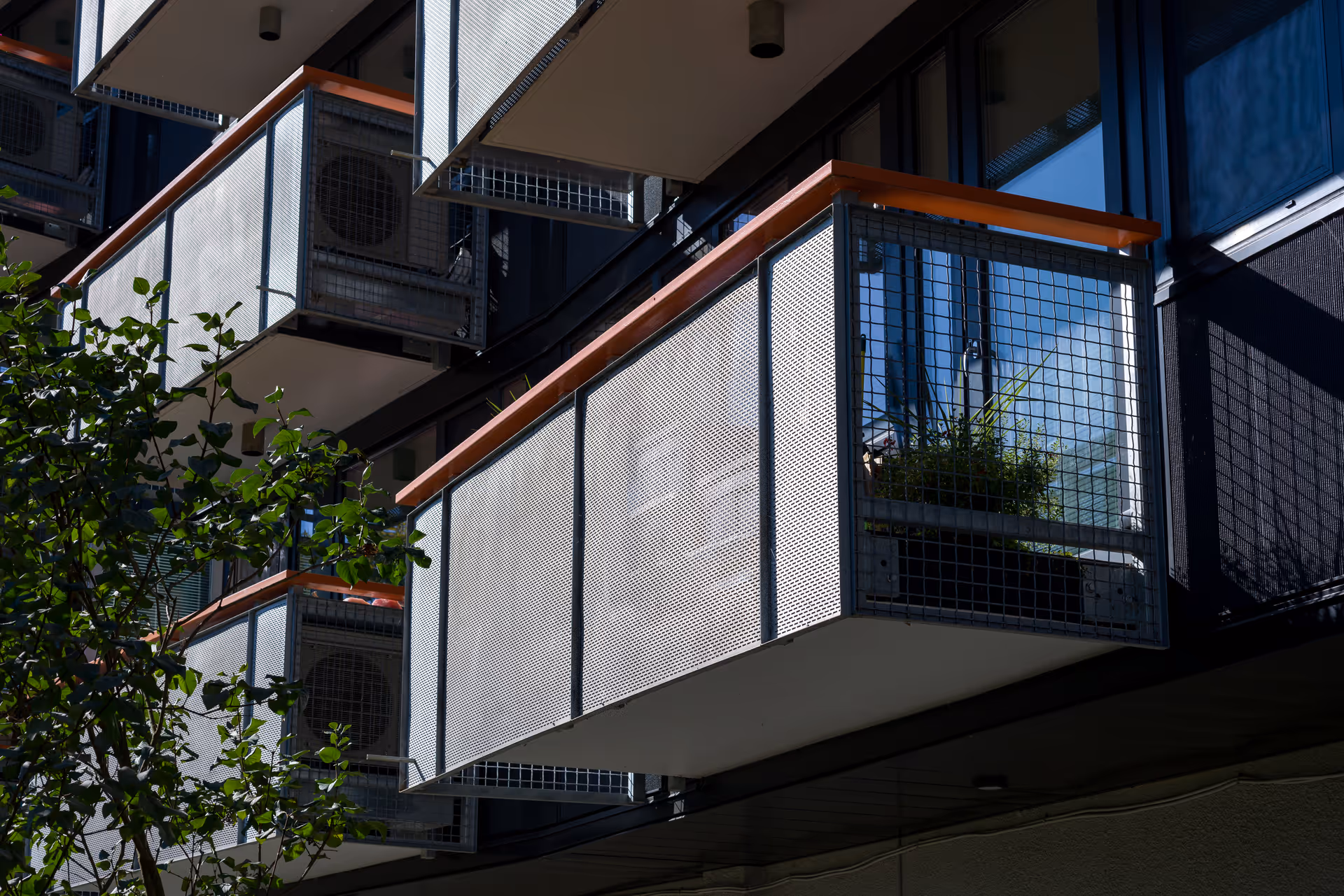 Close-up of modern apartment balconies with metal mesh railings and a potted plant.
