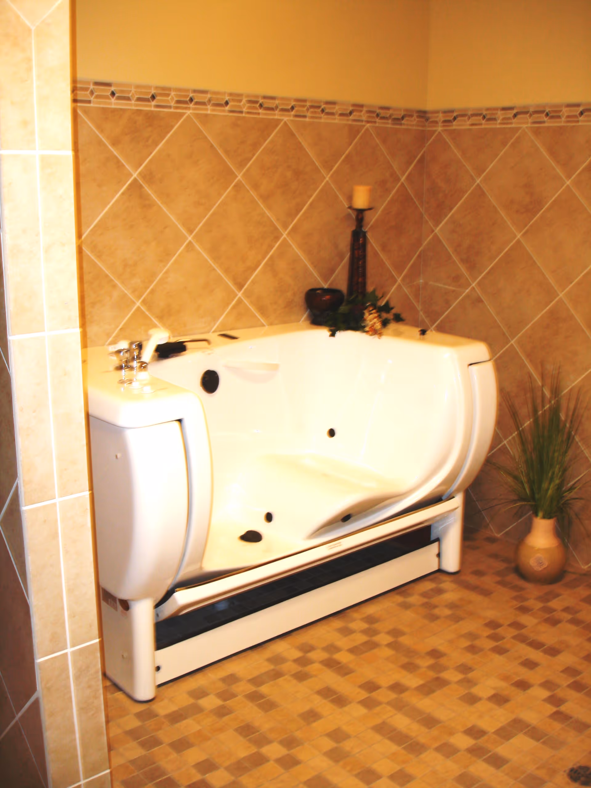 A white walk-in bathtub against beige tiled walls with a candle and a potted plant nearby.