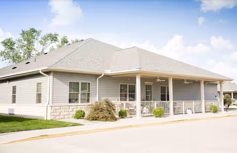 Single-story senior living facility exterior with a covered front porch and landscaping.