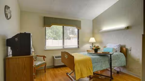 Patient room in a senior facility with an adjustable bed, TV, chair, and window.