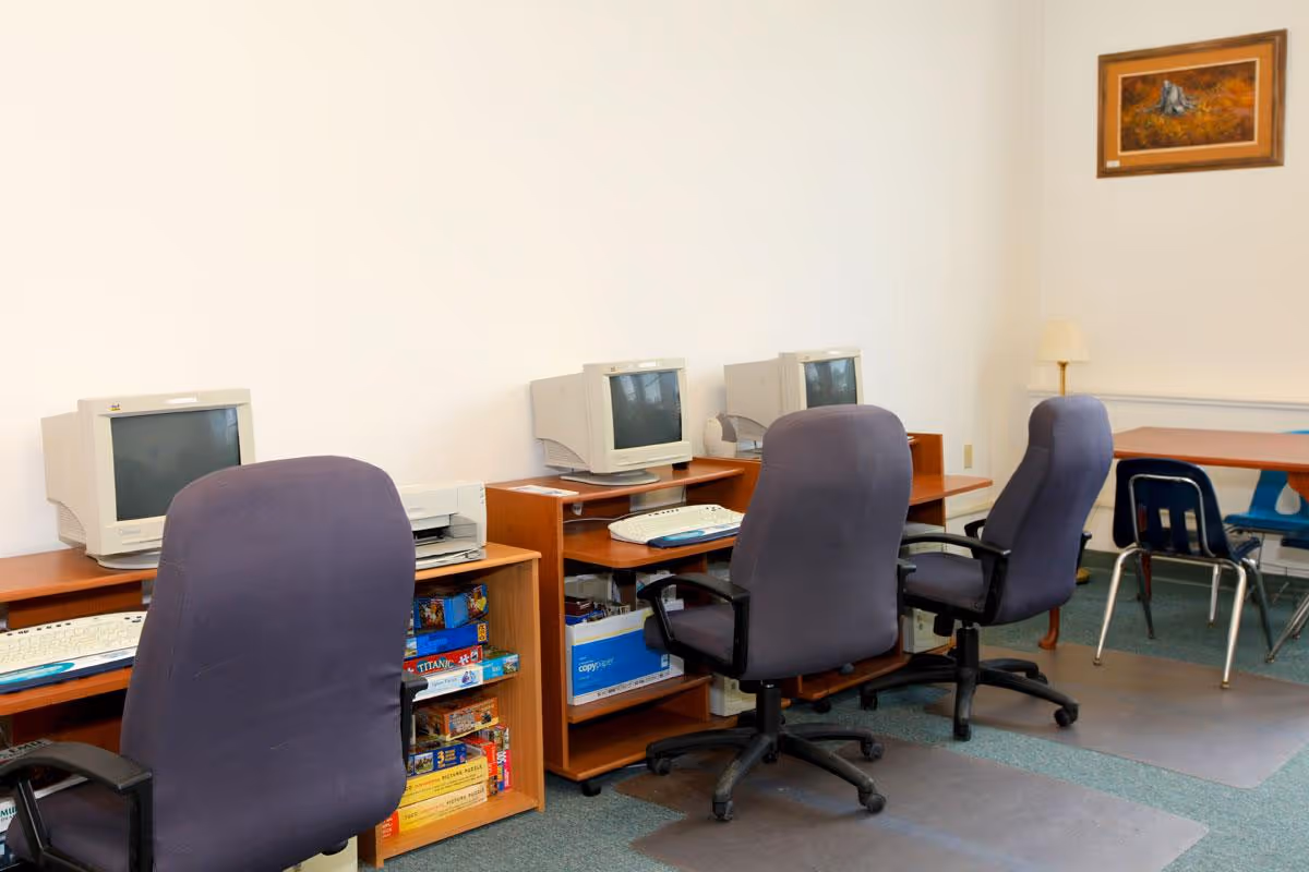 A small computer room with three CRT monitors on wooden desks and purple swivel chairs.