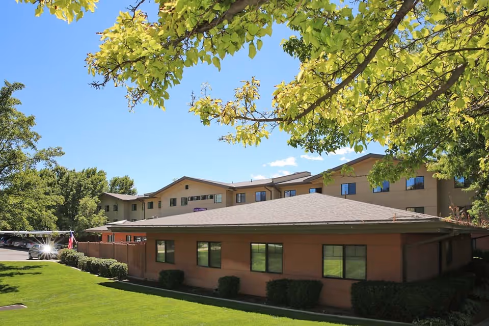 Exterior view of a multi-story senior living building with a green lawn and trees and a single-story brick wing in the foreground.