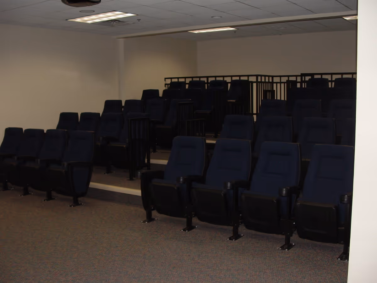 A small auditorium or theater room with multiple rows of dark blue cushioned seats arranged in a tiered layout inside a building.