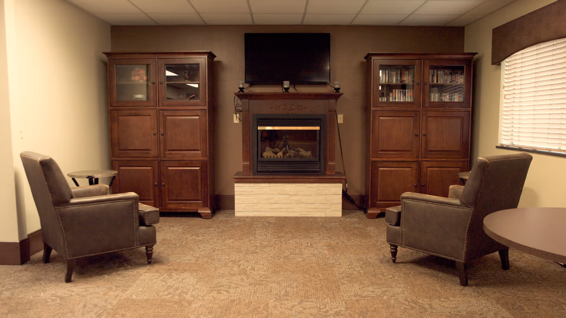 Cozy sitting area with two armchairs facing a fireplace flanked by wooden cabinets and a wall-mounted TV.