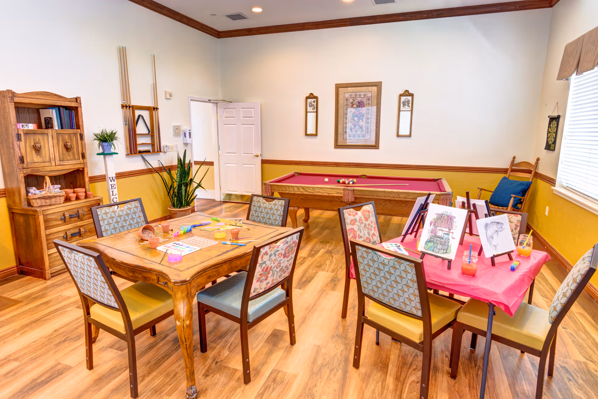 Community activity room with tables set for arts and crafts and a pool table in the background.