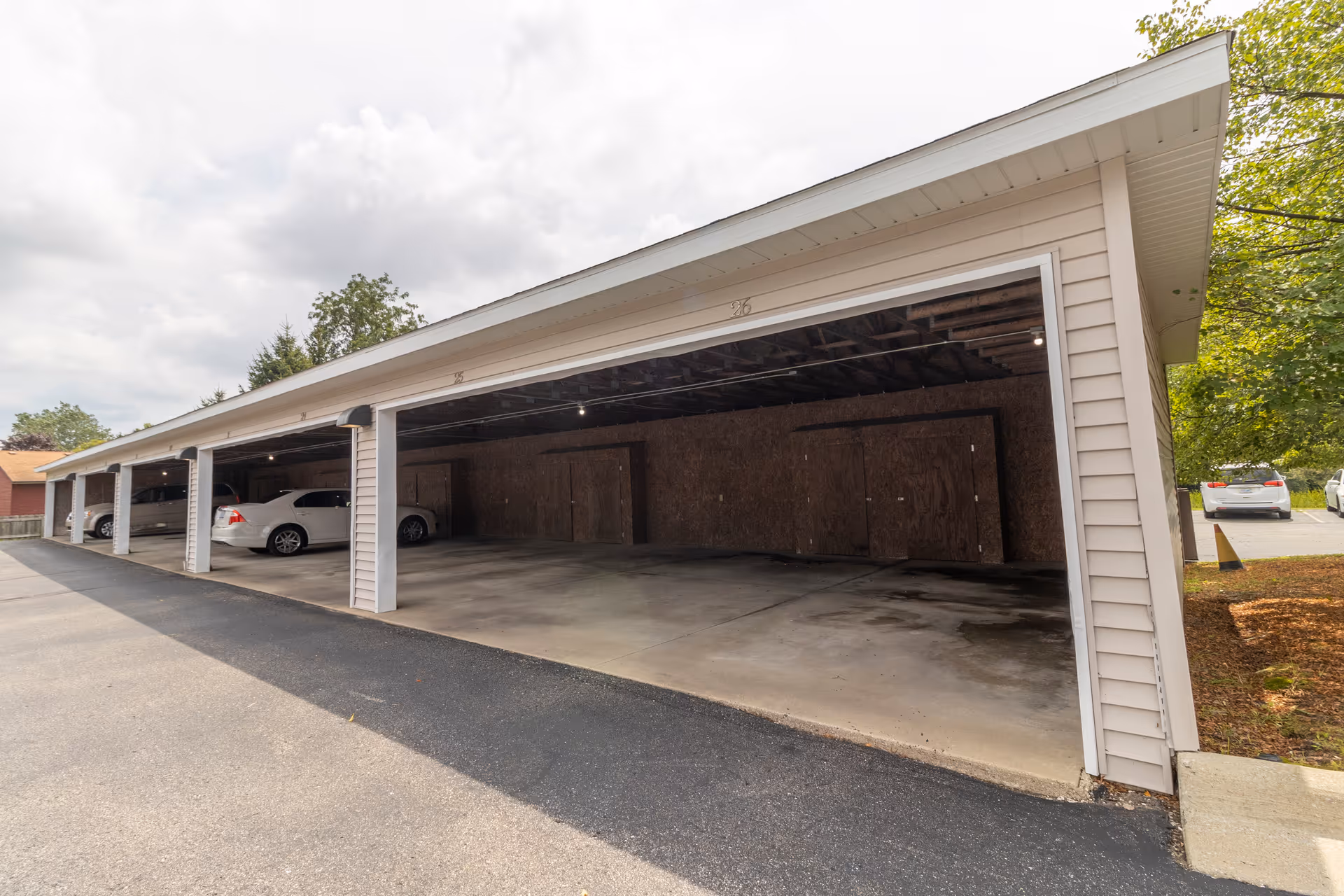 Covered carport with multiple open parking bays and a few parked cars beside a building.