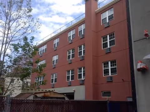 Multi-story red brick care center exterior with trees and a fence.