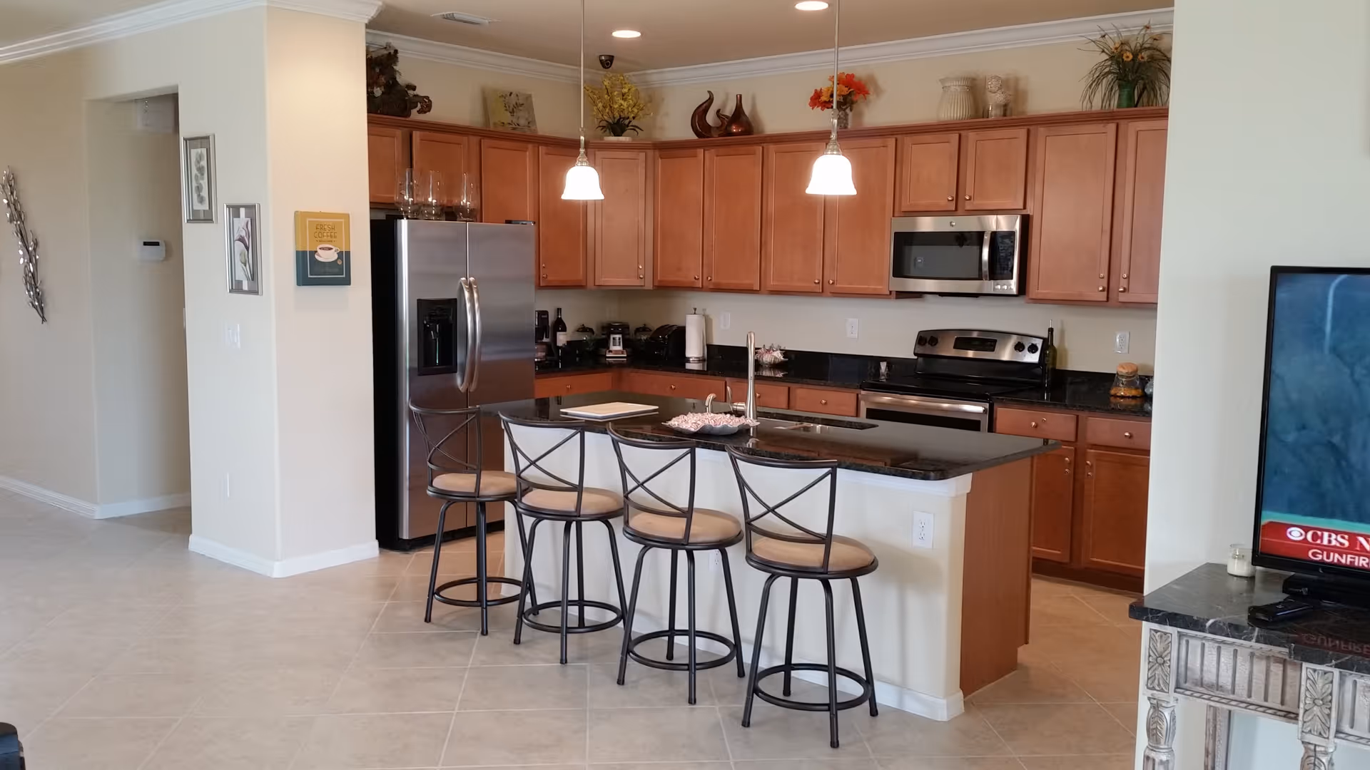 Open-plan kitchen with a central island and four bar stools, stainless steel appliances, and wooden cabinets.