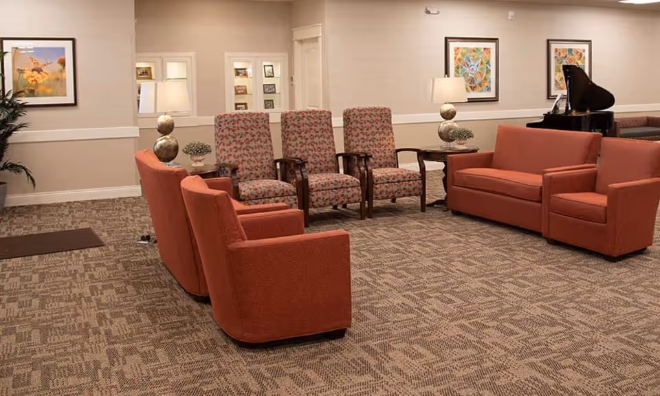 A spacious seating area with orange upholstered chairs and sofas arranged around side tables and framed artwork on the walls.