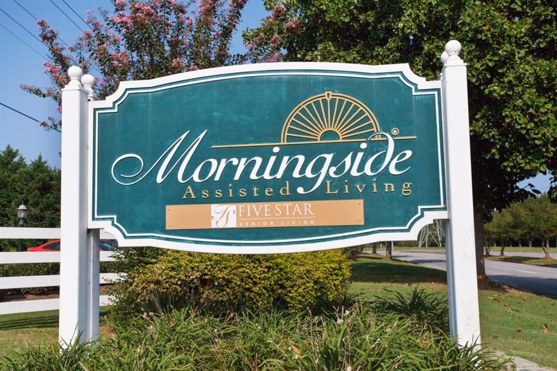 A green roadside sign reading "Morningside Assisted Living" with landscaping and trees in the background.