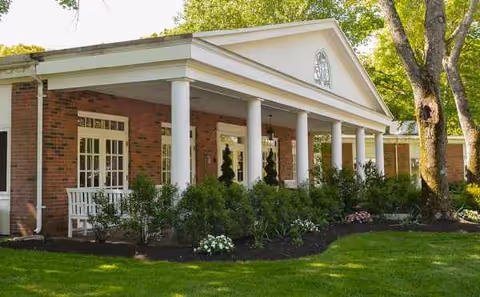 Queen Anne Nursing Home exterior with brick facade, white columns, and landscaped front lawn.