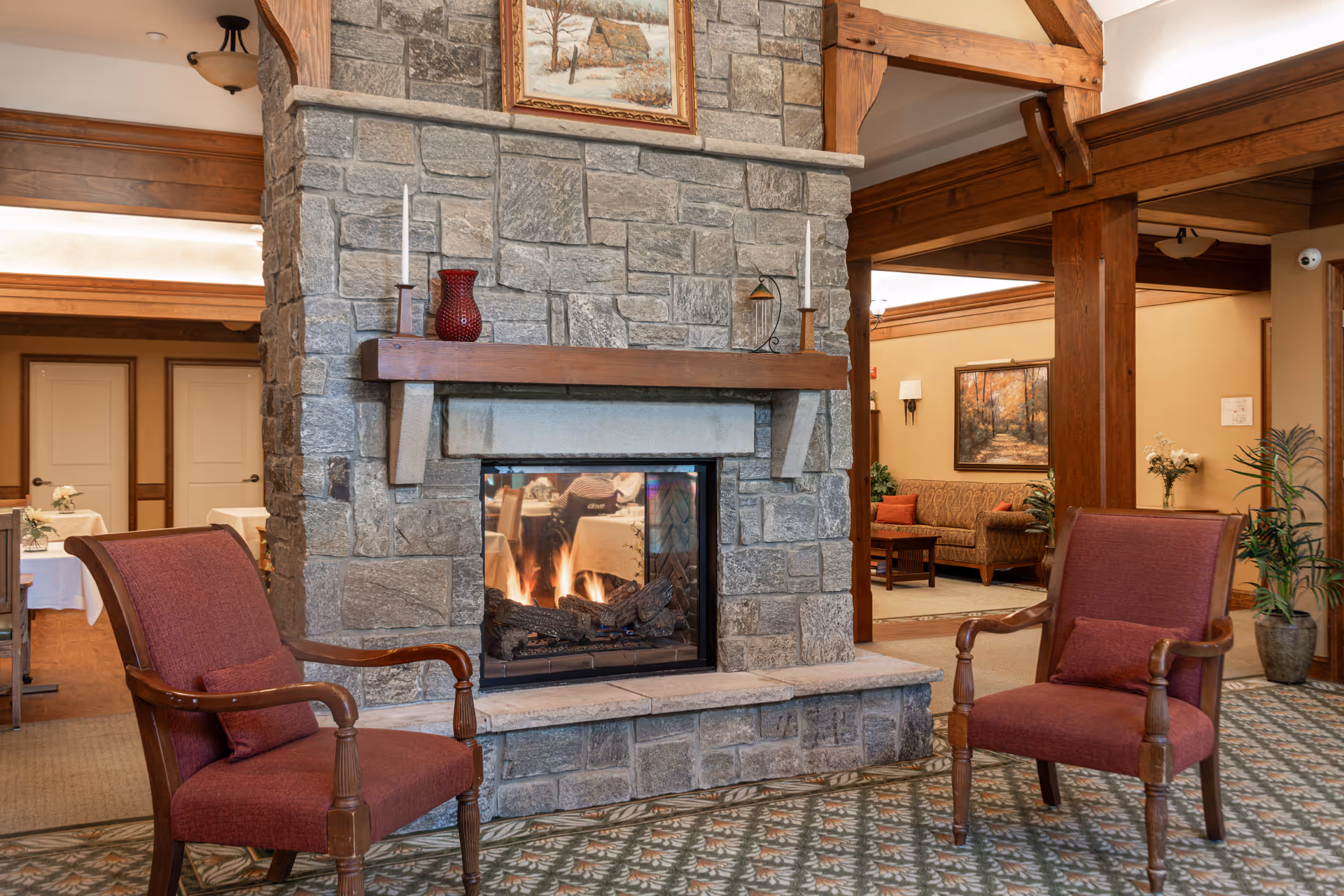 Cozy seating area with two red armchairs facing a stone fireplace in a senior living common room.