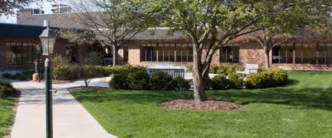 Exterior view of a brick senior care facility with a lawn and trees.