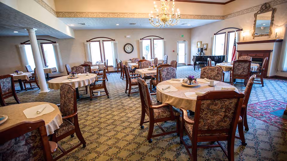 Large elegant dining room with round tables, floral-upholstered chairs, place settings, and a chandelier.