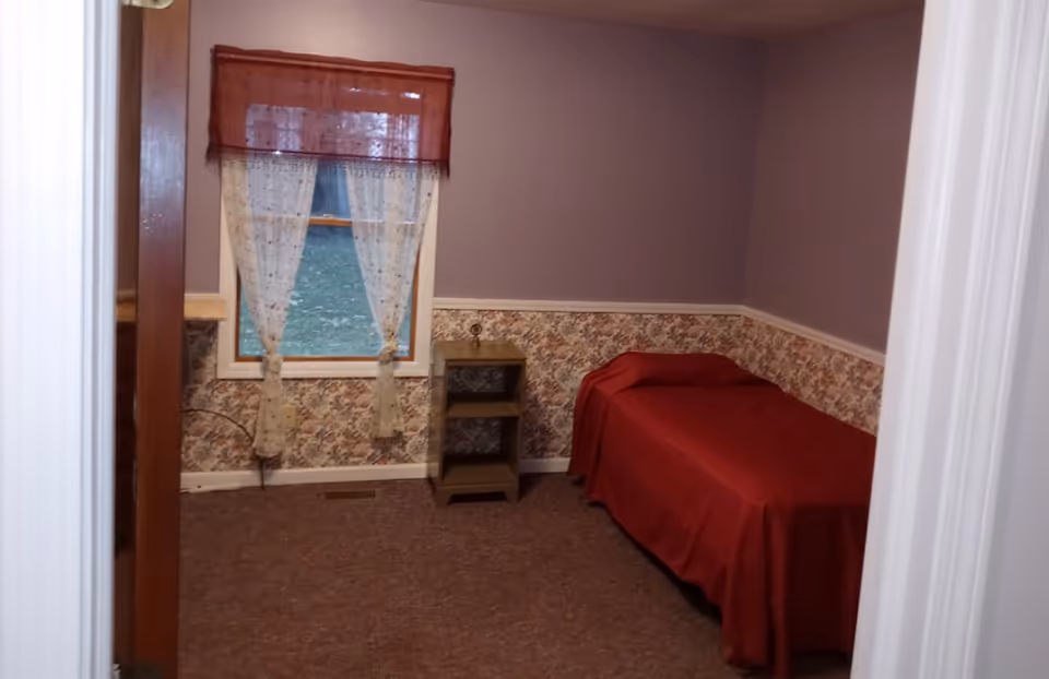 Purple-walled bedroom with a single bed, floral border, and window with sheer curtains.