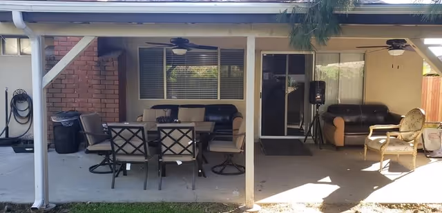 Covered outdoor patio area with a dining table, multiple chairs and sofas under a roof attached to the building.
