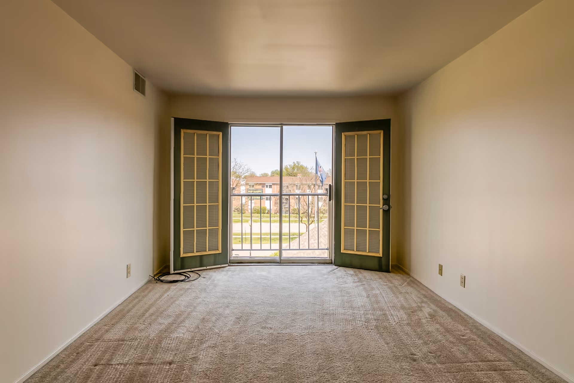 Empty carpeted living room with open French doors and a sliding glass door leading to a small balcony and outside view.