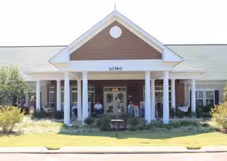 Front view of SomerOak Senior Living building with columns and residents near entrance.