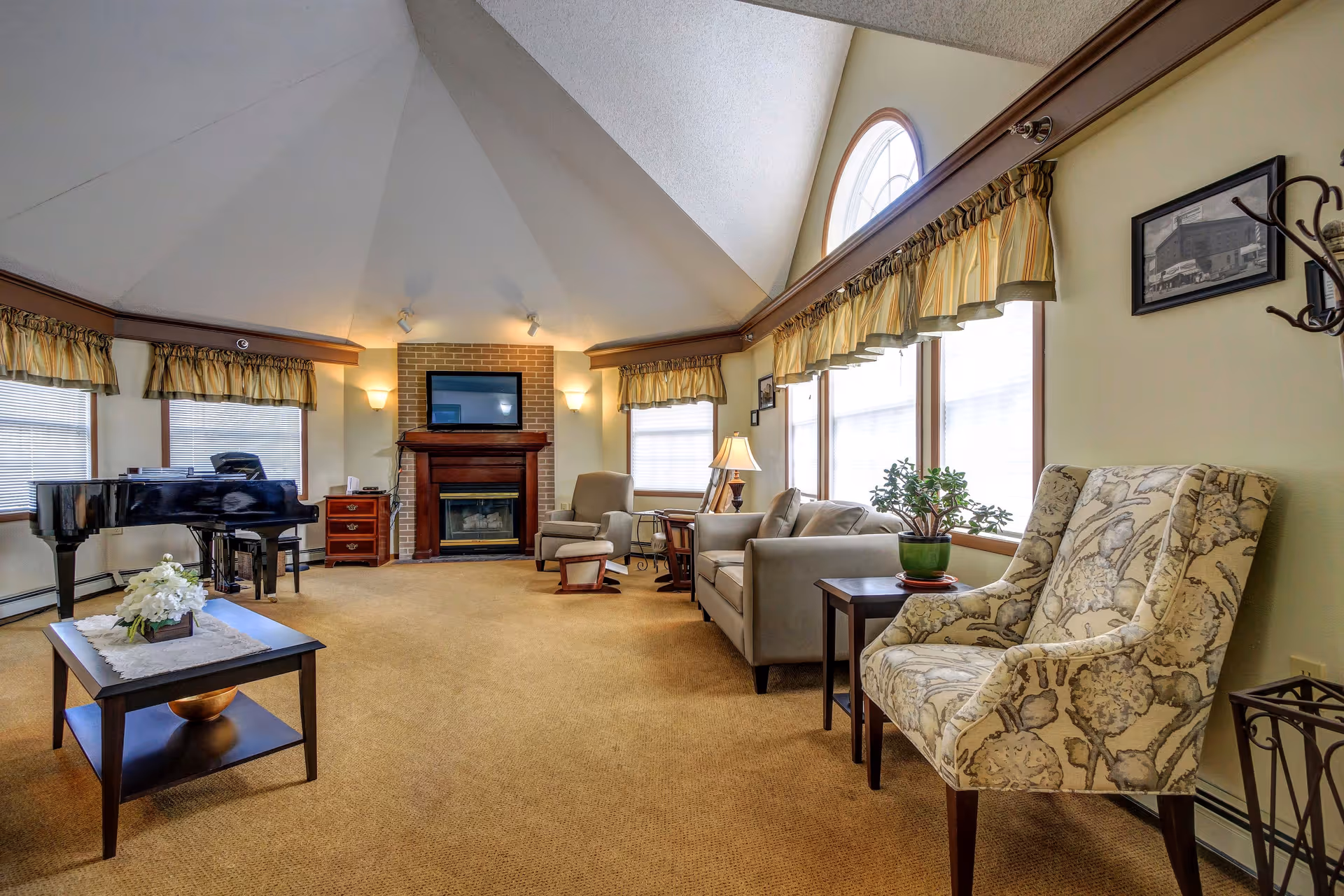Spacious sunlit lounge with a vaulted ceiling, fireplace, sofas, armchairs, and a grand piano.