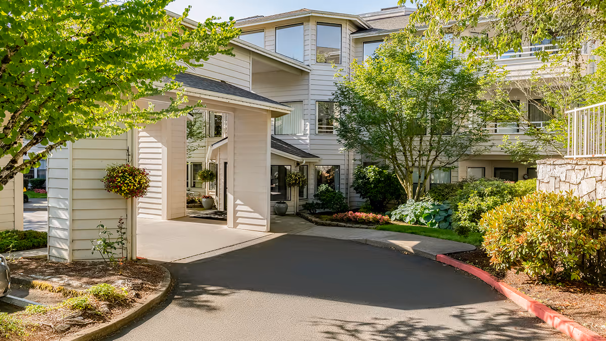 Front entrance and driveway of the Holiday Hidden Lakes building with a covered porte-cochere and landscaped trees and shrubs.
