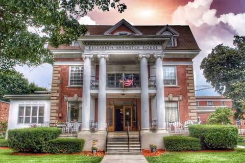 Brick building with four columns and steps, Elizabeth Brewster House, American flag, landscaped lawn.