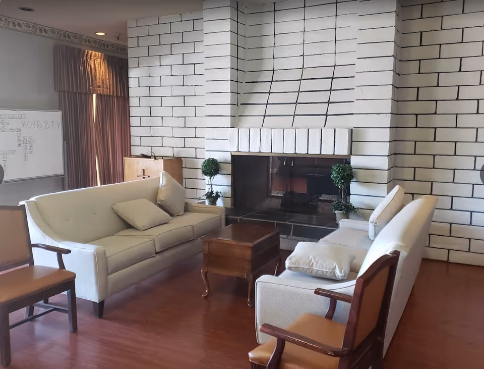 Living room-style lounge with two light-colored sofas, armchairs, a wooden coffee table, and a large white brick fireplace.
