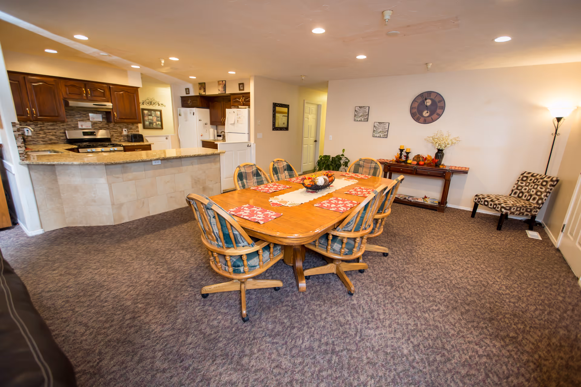 Open dining area with a wooden table and six chairs positioned in front of a kitchen with a breakfast bar.
