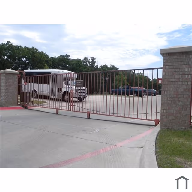 Gated parking entrance with a metal swing gate and a white shuttle bus parked inside the lot.