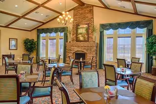A brick fireplace anchors a formal dining room with green curtains and neatly arranged tables.