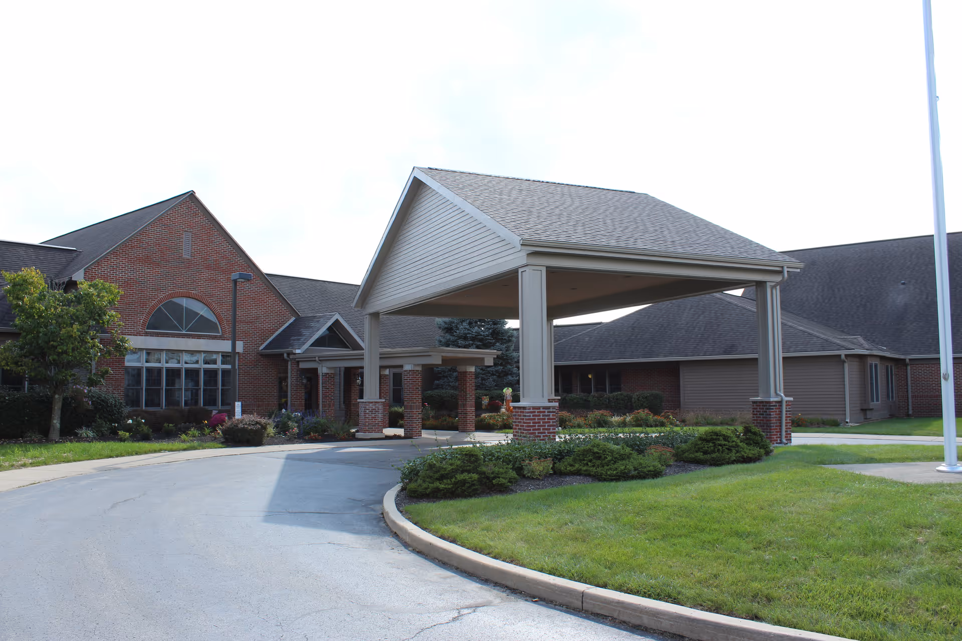 Exterior view of Garbry Ridge facility showing a covered entrance with brick pillars, a driveway, landscaped bushes, and a green lawn under a partly cloudy sky.