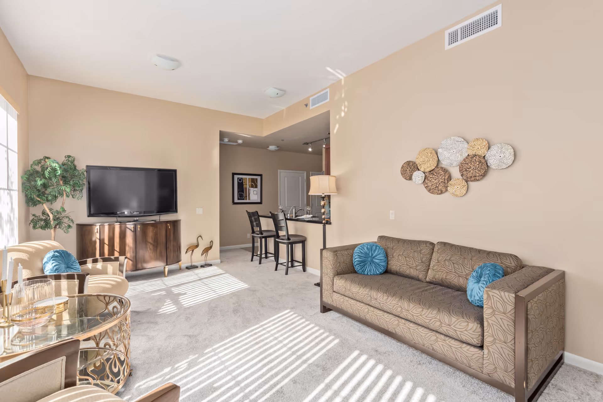 Bright living room area with beige walls, sofa, TV, and dining/bar seating.