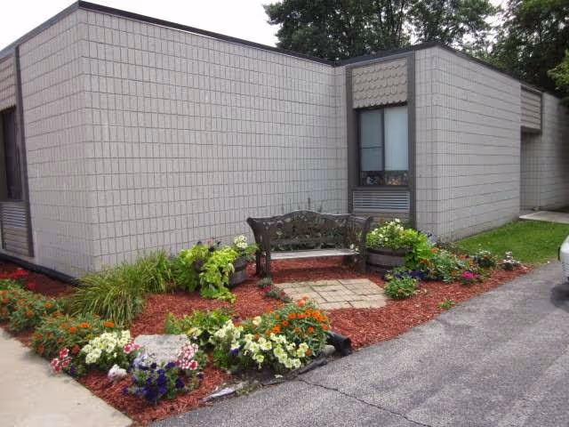Exterior corner of a single-story building with a bench and landscaped flower beds.