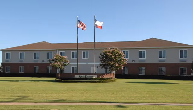 Exterior view of Royal Estates of Wichita Falls, a two-story senior living facility with flags.