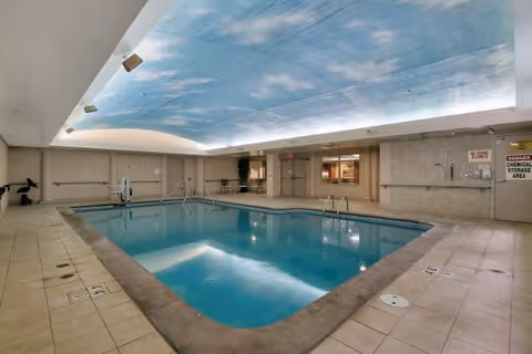Indoor swimming pool with tiled deck and a sky-painted ceiling inside a senior living facility.