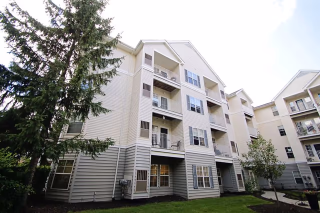 Exterior view of a multi-story beige apartment building with balconies, windows, and landscaped lawn.