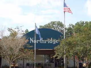 Front exterior of a building with a blue arched sign and flag amid trees.