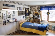 A single bed in a small, sports-themed resident bedroom decorated with New York Yankees and West Virginia Mountaineers memorabilia, a lamp, and a window with a blue valance.