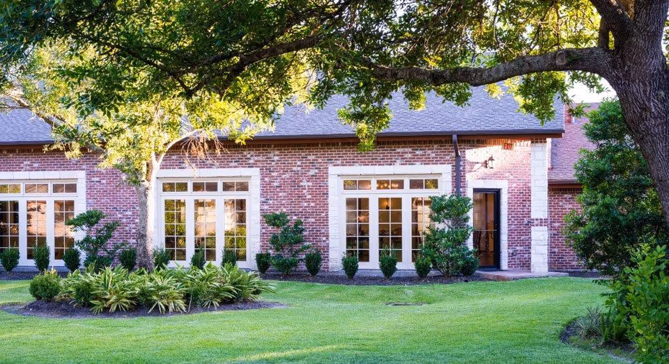 Brick single-story building with large glass doors and windows opening onto a manicured lawn, trees, and shrubs.