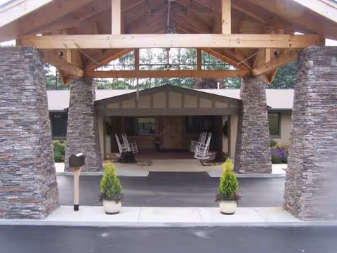 Stone pillars frame a wooden entry with a covered porte-cochère and rocking chairs.