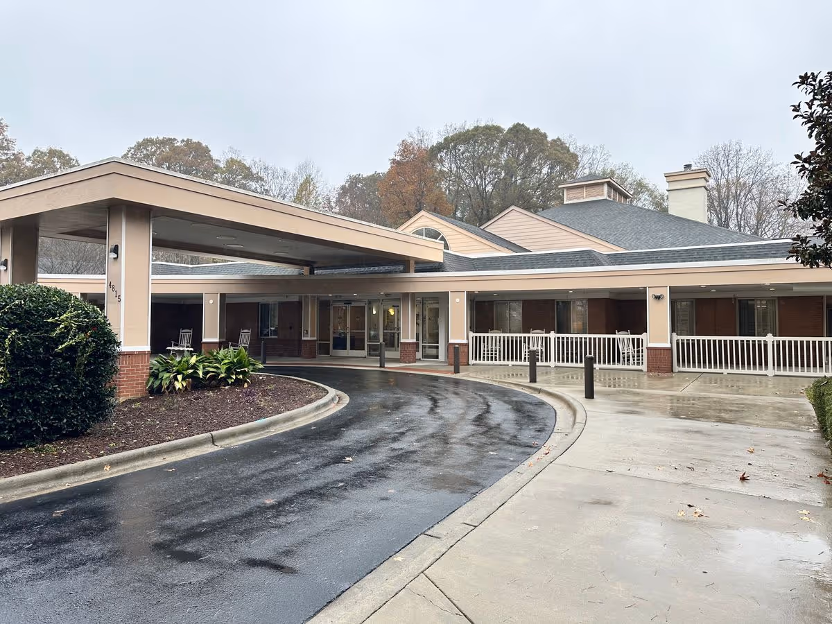 Front entrance of a senior living building with a covered porte-cochère, curved wet driveway, and a porch with railings.
