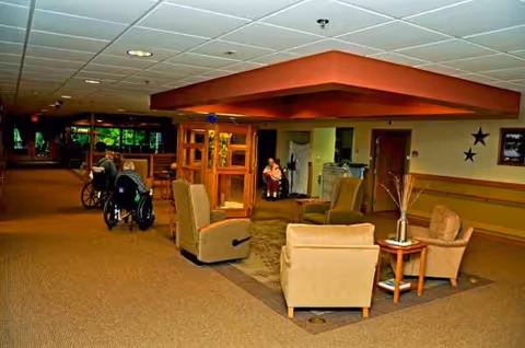 Interior lounge with beige seating, tables, and wheelchairs in a senior living facility.
