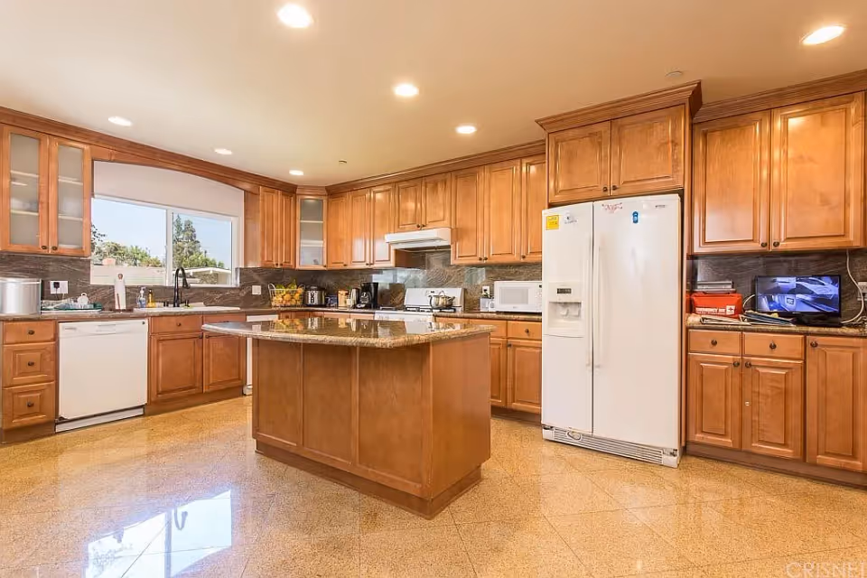 Spacious kitchen with wooden cabinets, a central island, white refrigerator and dishwasher, and recessed lighting.