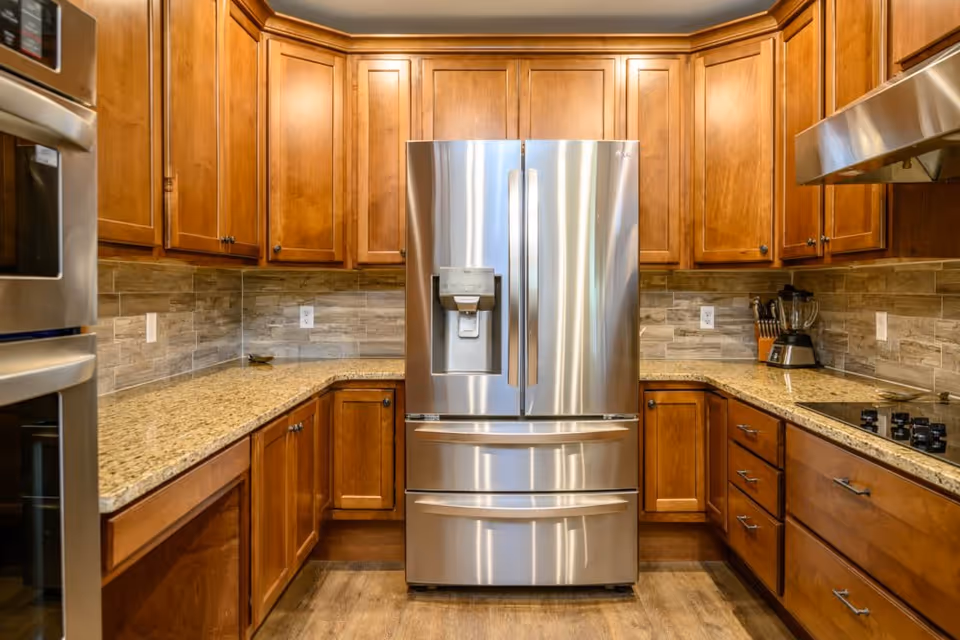 Modern kitchen with a stainless steel French-door refrigerator centered between wooden cabinets and granite countertops.