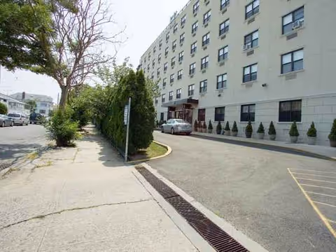 Exterior view of a multi-story senior living building with a driveway and shrubs.