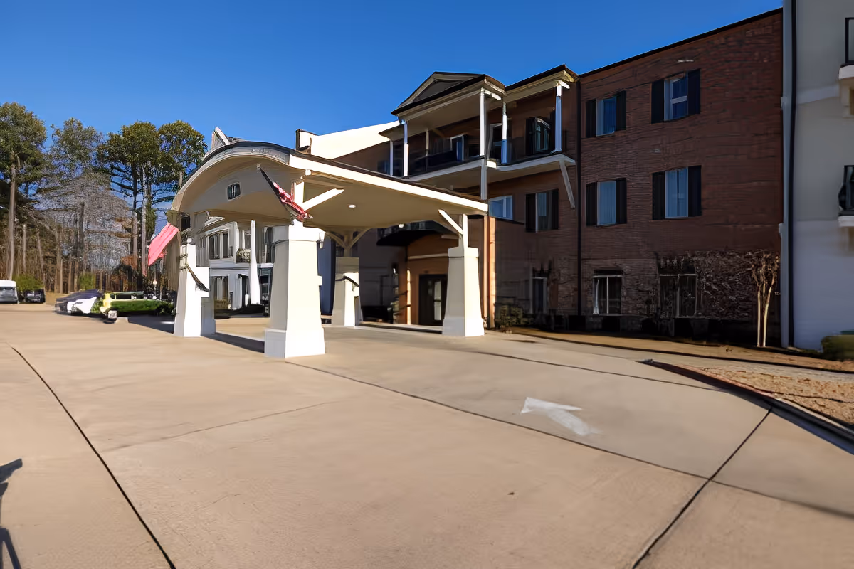 Front entrance and porte-cochere of a multi-story senior living facility with American flags and a curved driveway.