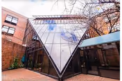 Glass pyramid-shaped entrance framed by brick buildings and a courtyard path.