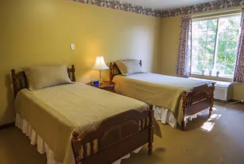 Two single beds in a warm shared bedroom with a nightstand and window.