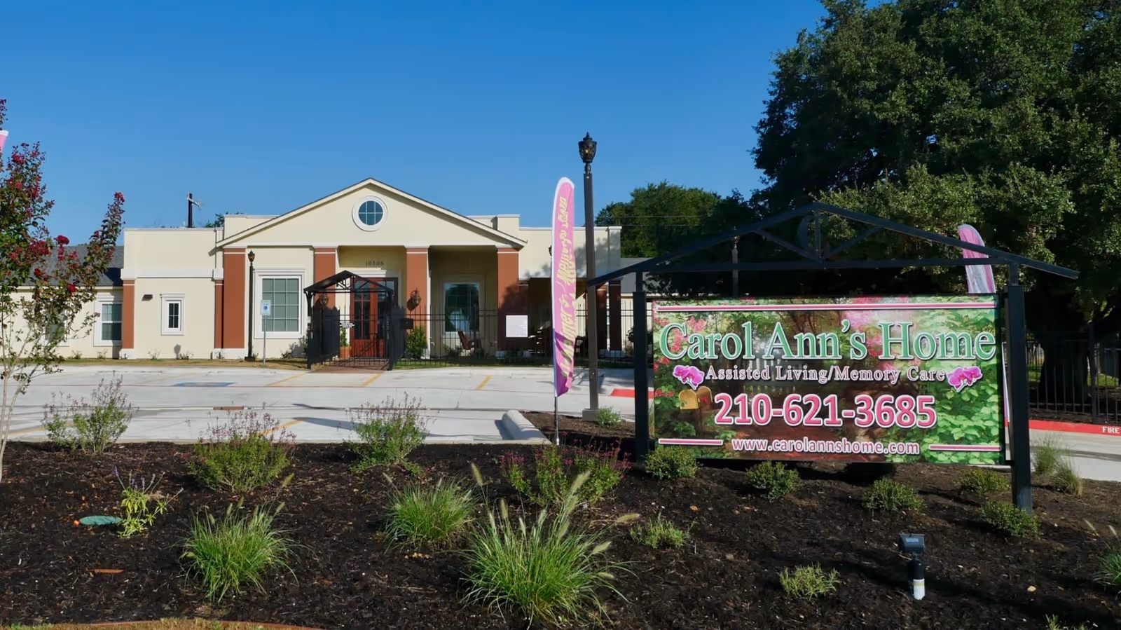 Front exterior of Carol Ann's Home assisted living building with a landscaped entrance and a large sign displaying the facility name and phone number.