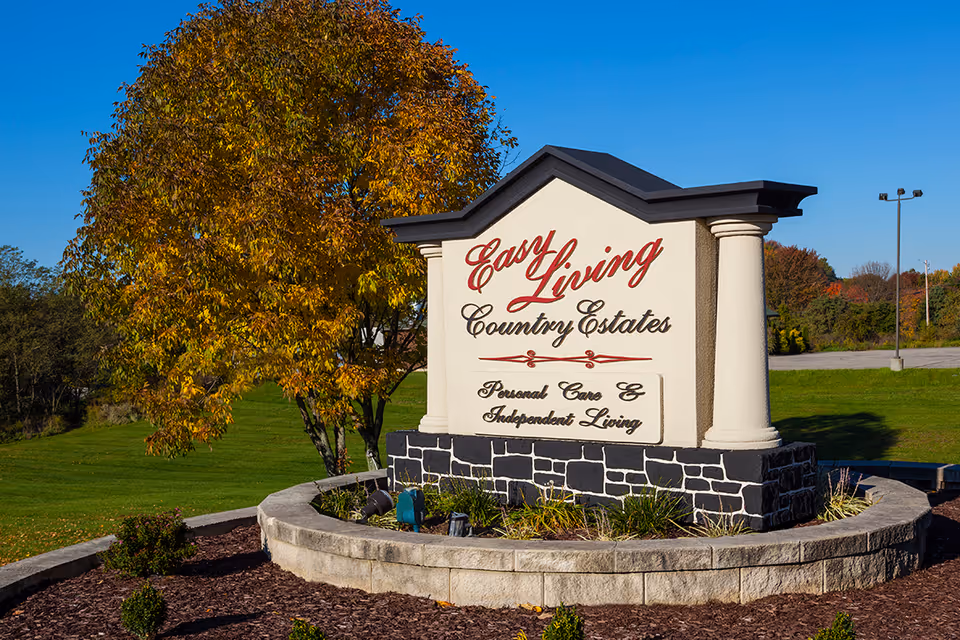 Entrance monument sign for "Easy Living Country Estates" on a landscaped lawn with a tree and clear blue sky.